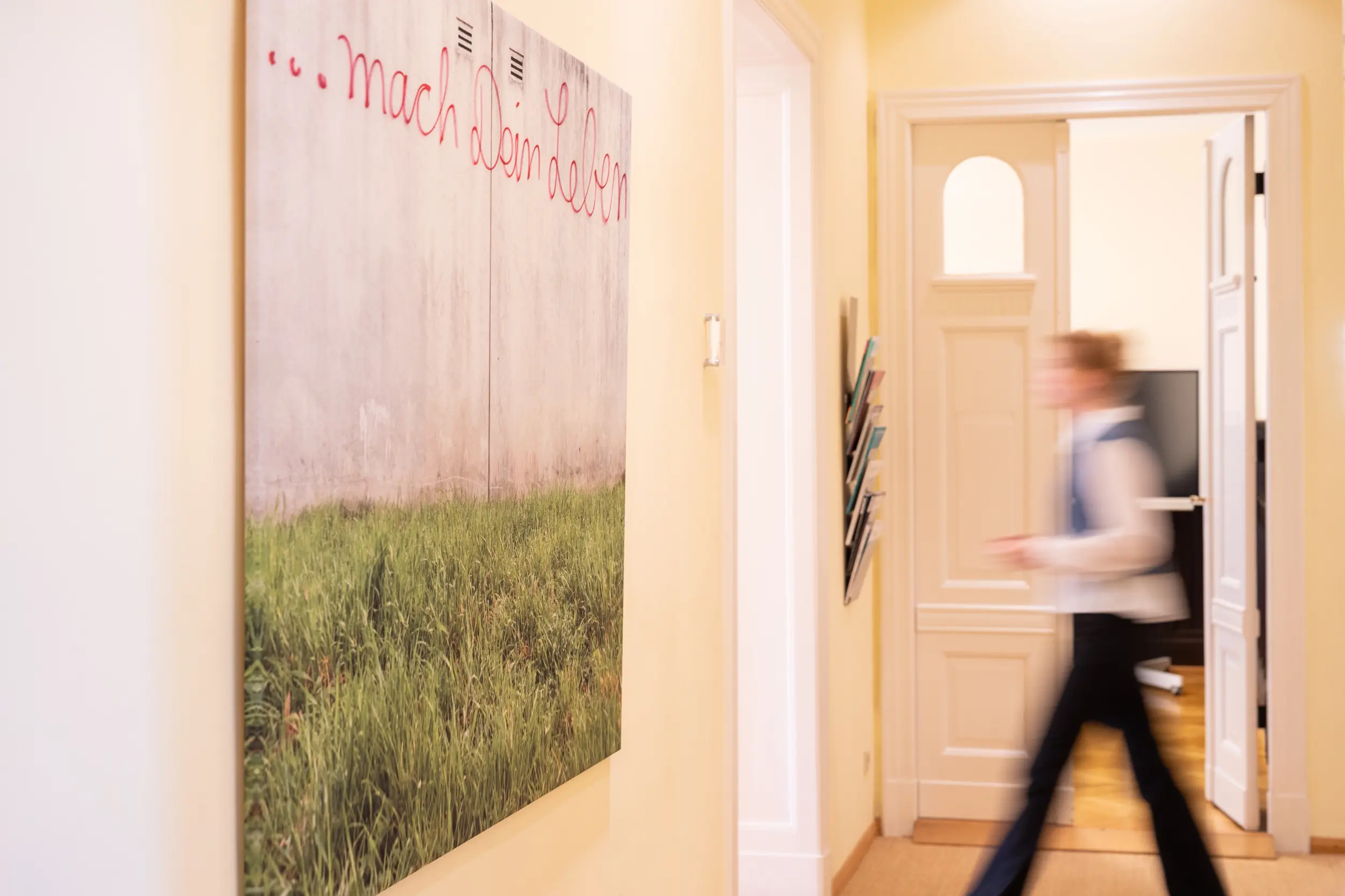 Outplacement für Führungskräfte - OMC Berlin Büroflur mit dem Leitmotiv mach Dein Leben – symbolisch für Neuanfang und Karriereberatung. Junge Frau läuft durch das Bild, leicht verschwommen.