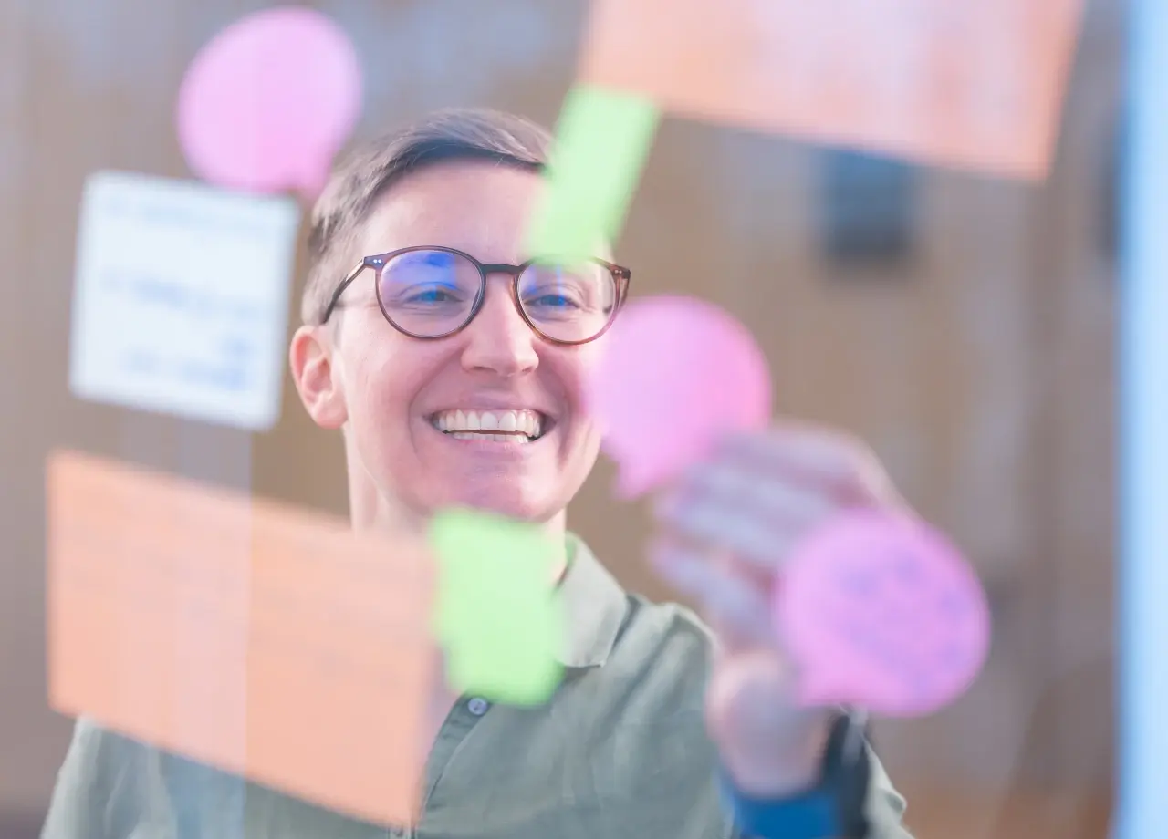 Frau klebt Post-it an Glaswand während eines Karriereberatungs-Workshops bei OMC Berlin