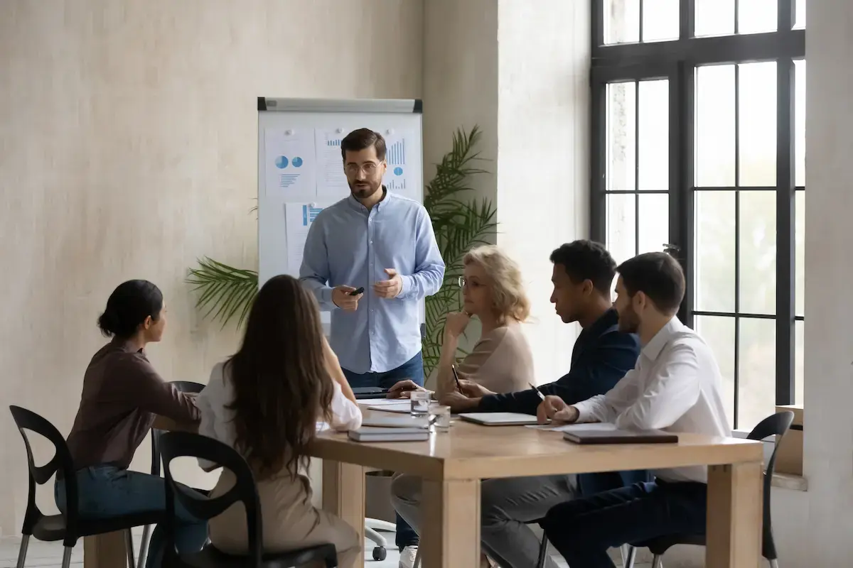 OMC-Berater präsentiert Analyse-Charts am Flipchart vor einem aufmerksamen diversen Team – professioneller Workshop in modernem Meetingraum