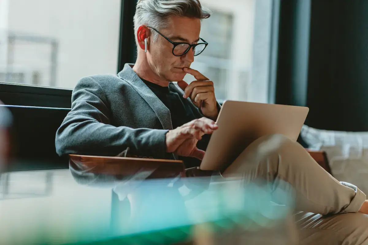 Erfahrener OMC-Berater konzentriert am Laptop im modernen Loungebereich – fokussierte Analyse mit AirPods in entspannter Arbeitsatmosphäre